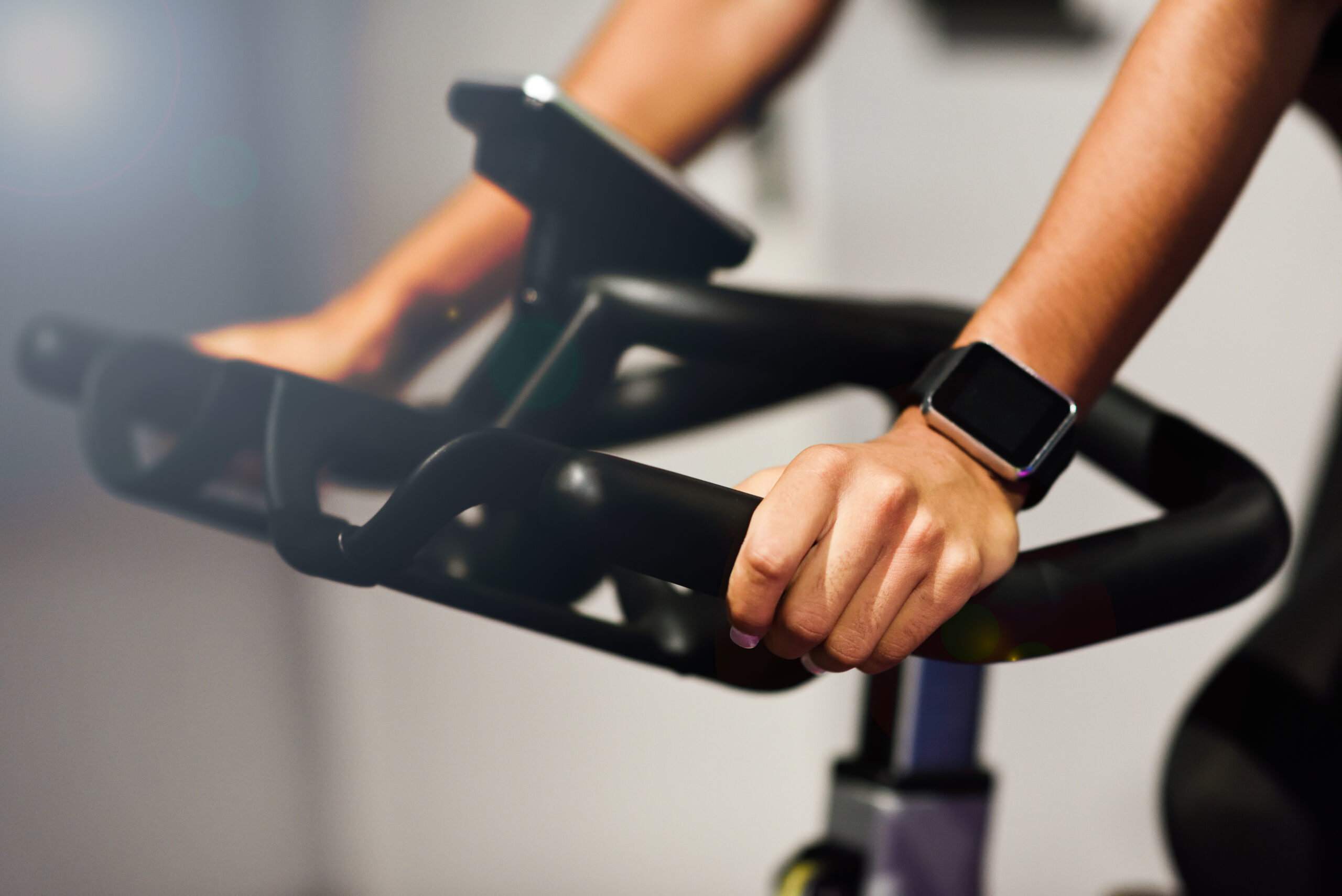 Hands of a woman training at a gym doing spinning or cyclo indoor with smart watch. Sports and fitness concept.